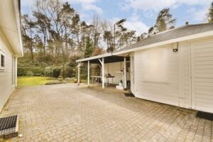 a garage with a brick driveway and a white house