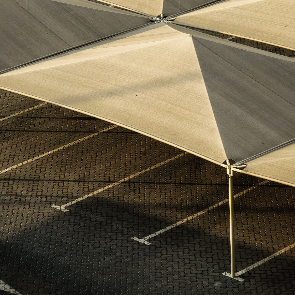 Structure d'ombrage contemporaine projetant des ombres marquées sur un parking en plein soleil