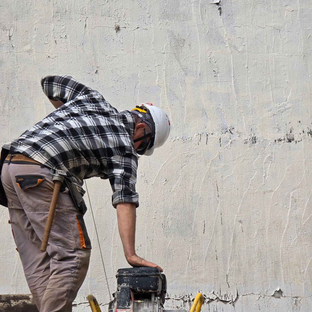 Ouvrier casqué travaillant à la machine sur un chantier extérieur le long d'un mur texturé