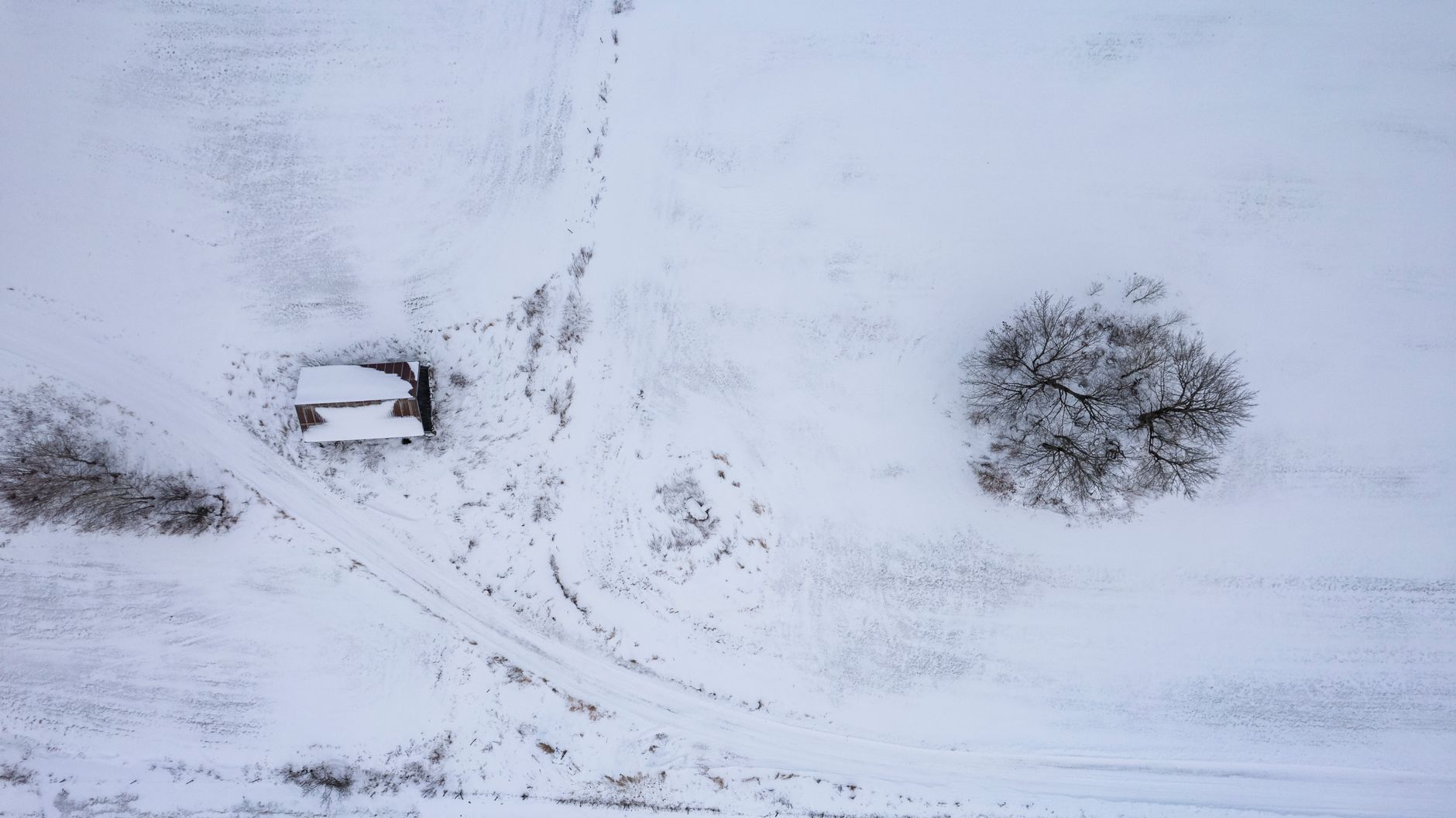 Champ enneigé vu du ciel avec une petite cabane sous la neige, image de l'accumulation de neige lourde à supporter par une structure