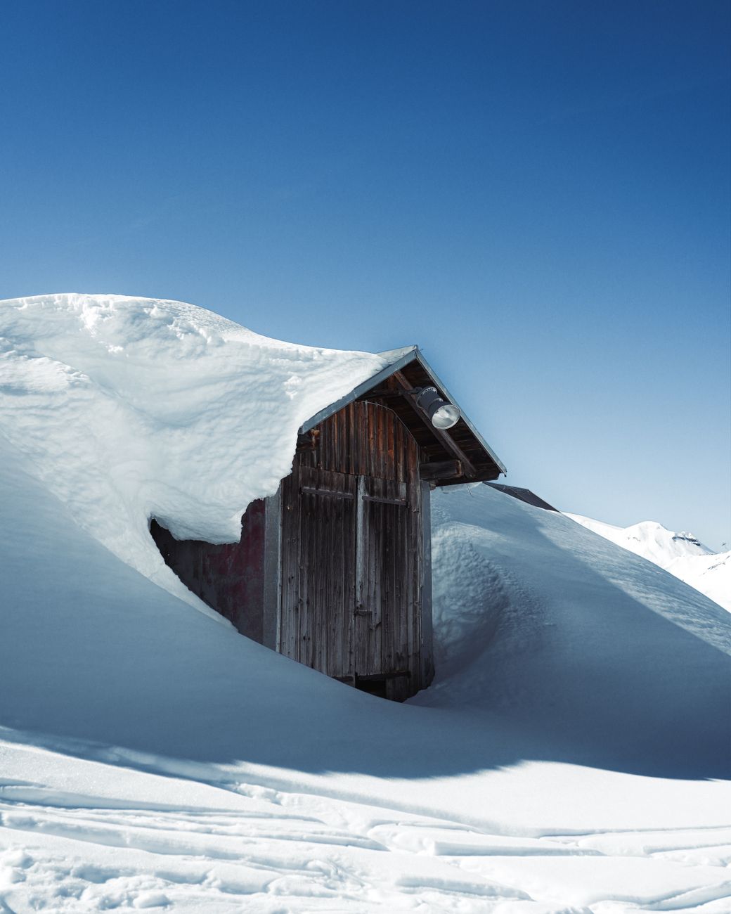 Chalet en bois sous une épaisse couche de neige et ciel bleu en altitude, contexte du Haut-Doubs pour une fenêtre sur mesure performante