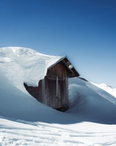 Chalet de montagne enseveli sous une épaisse couche de neige, illustrant l'enjeu climatique d'une pergola aluminium sur mesure dans le Haut-Doubs
