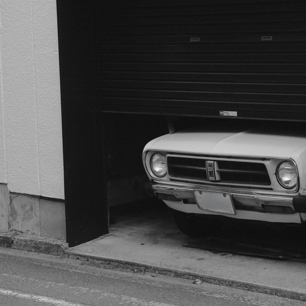 Voiture ancienne partiellement cachée sous une porte de garage en panneaux articulés