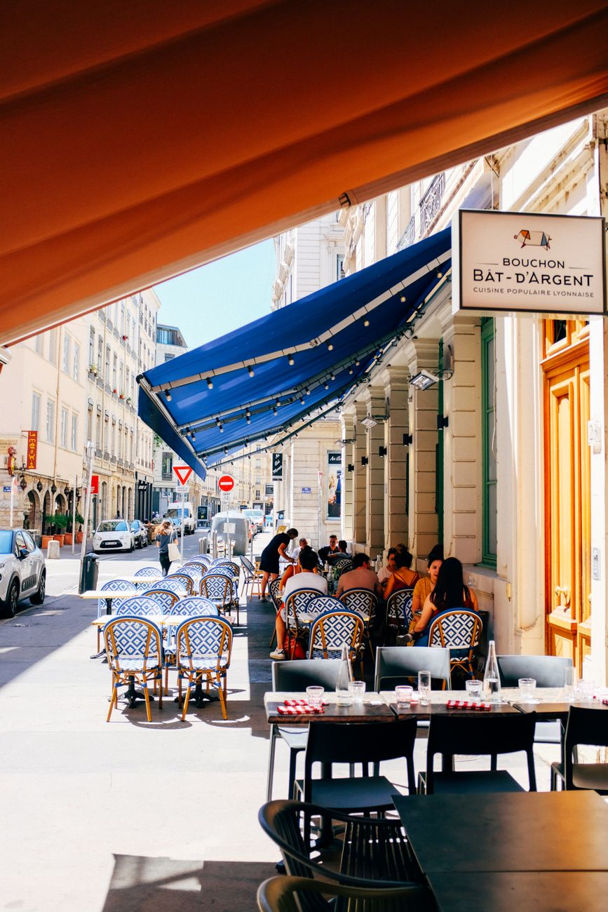 Terrasse de bistrot ombragée par un store banne, façade de restaurant en bord de rue